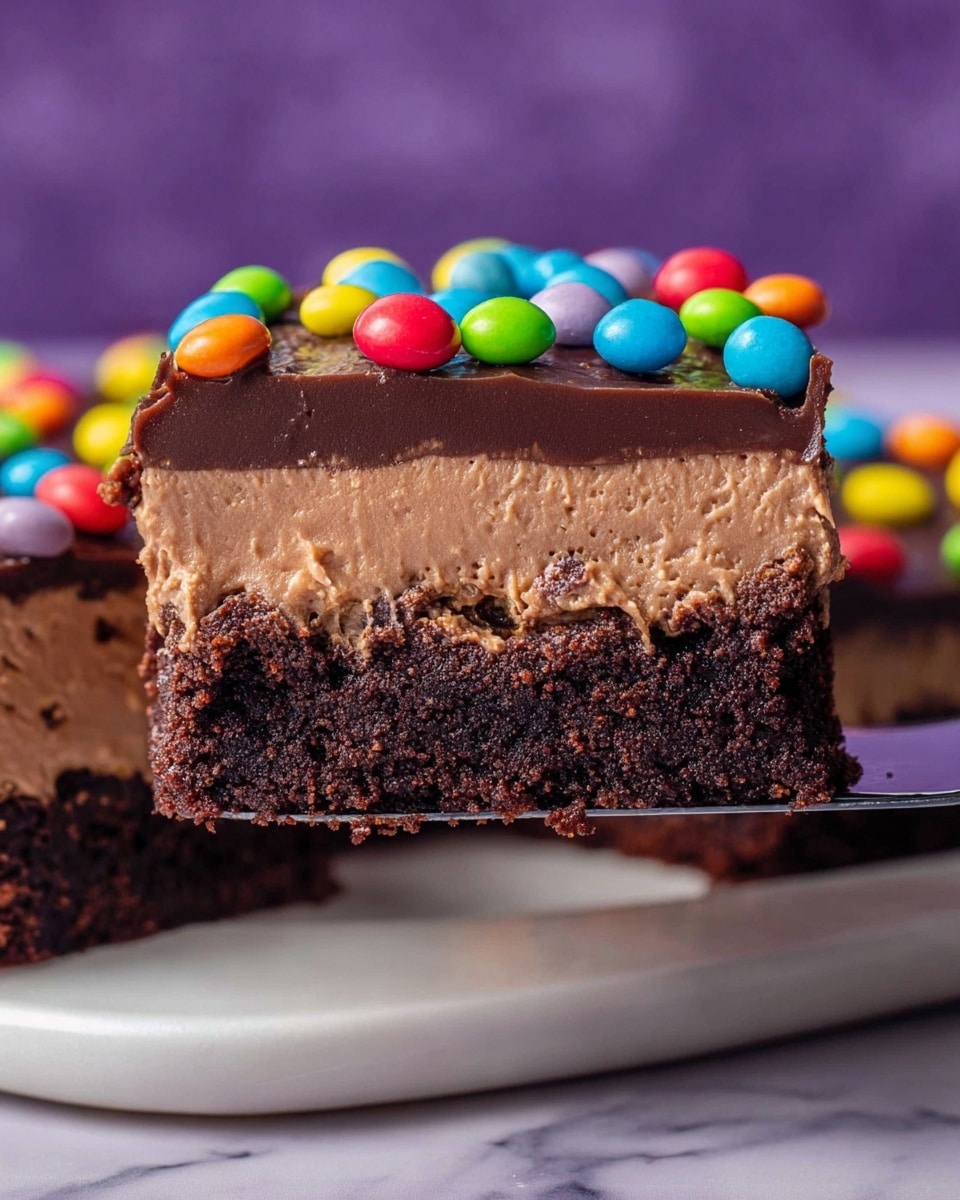 A close-up of a square piece of layered dessert being lifted by a spatula. The bottom layer is a dense, dark chocolate brownie with a moist texture. Above it is a thick, smooth outer layer of light brown chocolate mousse. Covering the mousse is a glossy, dark chocolate ganache layer. The top is decorated with small, round, colorful candy-coated chocolate pieces in bright colors like red, green, blue, yellow, orange, and pink. The dessert sits on a white plate, set on a white marbled surface with a purple blurred background. photo taken with an iphone --ar 4:5 --v 7
