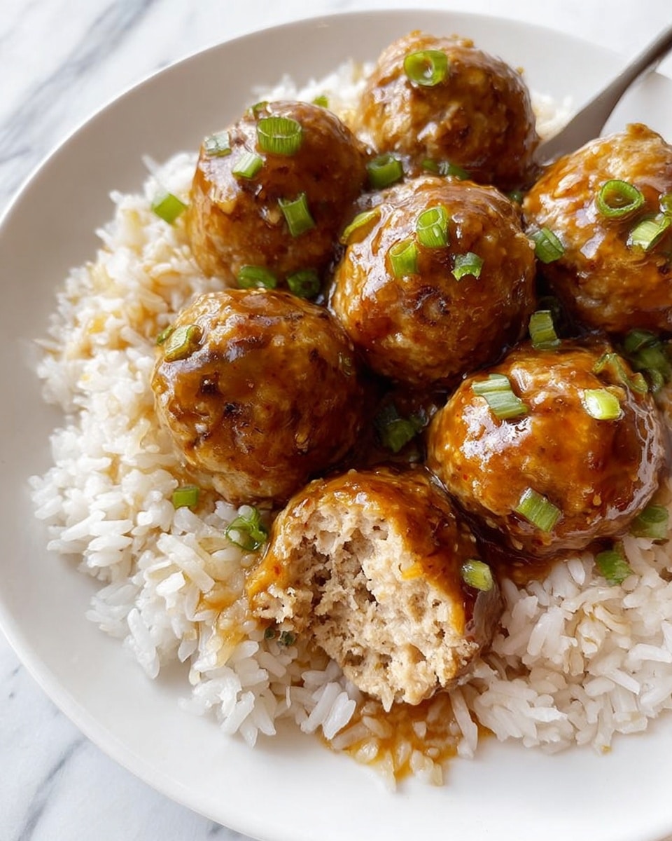A white plate holds a bed of cooked white rice as the bottom layer, with lightly separated grains visible. On top, there are seven golden-brown meatballs covered in a shiny, thick brown sauce that glistens with a glossy texture. Small bits of green onion are scattered on the meatballs, adding a fresh touch of green color. One meatball in the front has a bite taken out, showing a soft, light beige inside with a tender texture. The background is a white marbled surface. Photo taken with an iphone --ar 4:5 --v 7