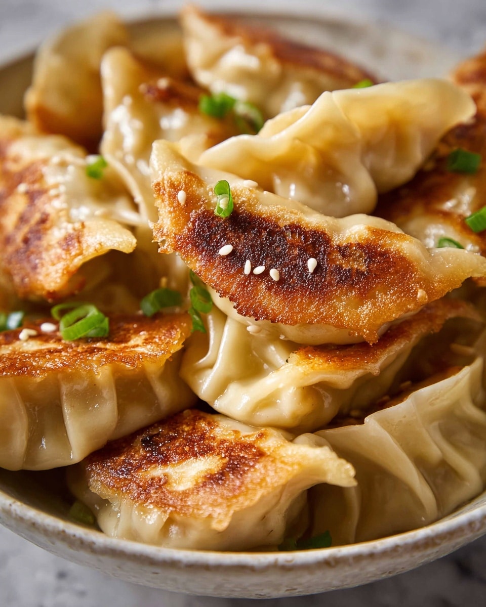 A close-up view of a pile of golden-brown pan-fried dumplings stacked in a white bowl, showing seven to eight dumplings with slightly crisp browned bottoms and soft, light beige tops. The dumplings have smooth, slightly shiny dough with fine pleated edges. Scattered small white sesame seeds and finely chopped green scallion pieces add texture and fresh color contrast on top. The background is a white marbled surface, enhancing the warm tones of the dumplings. photo taken with an iphone --ar 4:5 --v 7