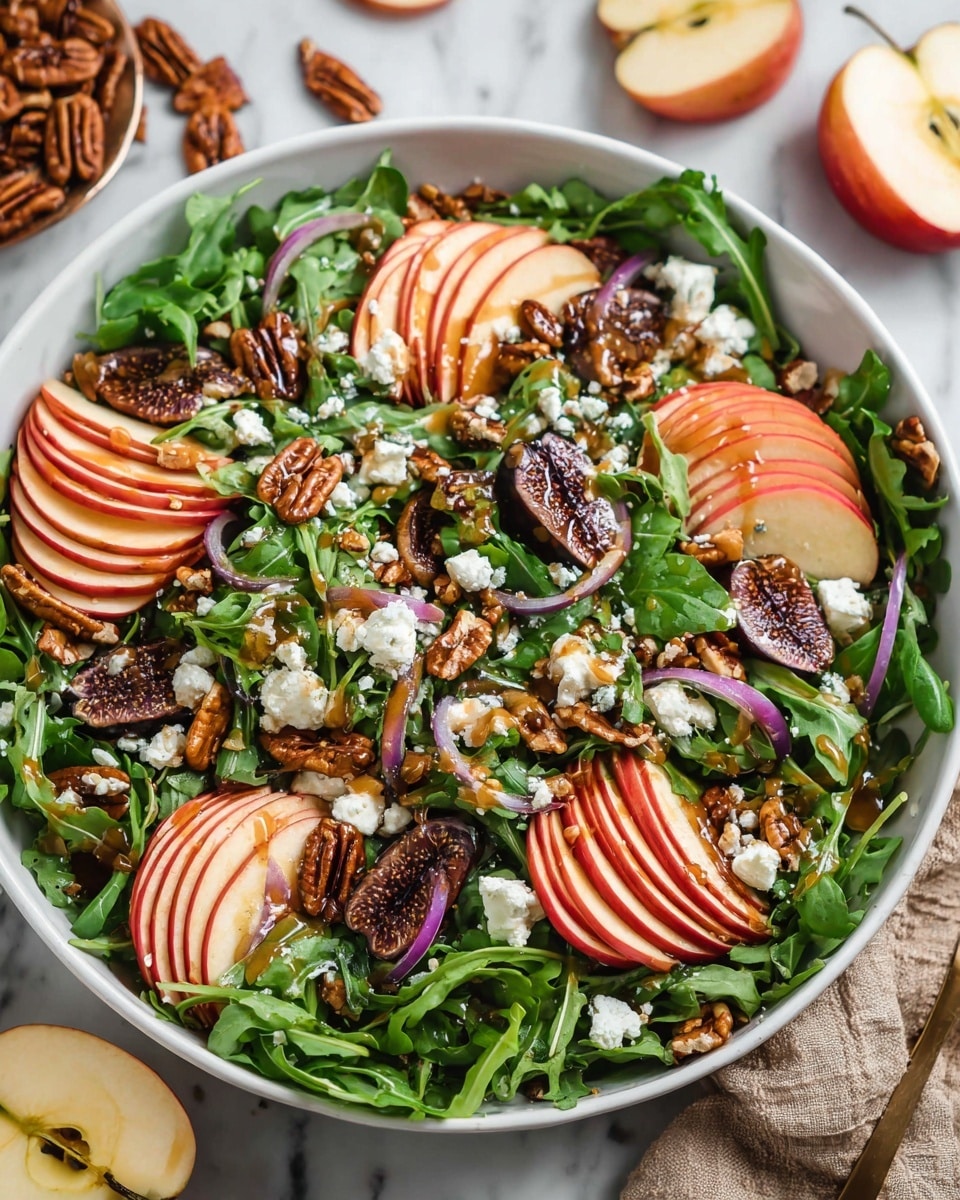 A white bowl filled with a fresh salad. The bottom layer is green arugula leaves spread evenly. On top, there are thin, curved slices of red-skinned apple arranged in small groups around the bowl. Scattered between the apple slices are whole pecan nuts with a glossy brown color. There are also small pieces of dried figs showing a dark brown inside with tiny seeds. Thin slices of purple onion are dispersed throughout. White crumbled cheese is sprinkled on top, and a light brown dressing is drizzled over everything. The bowl sits on a white marbled surface with some apple halves and pecans nearby. photo taken with an iphone --ar 4:5 --v 7