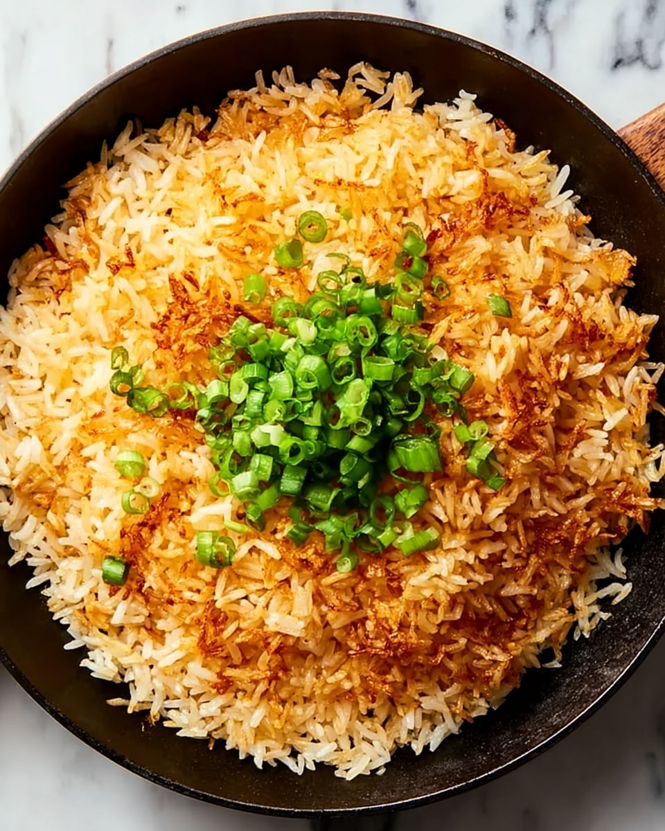 A close-up of a black skillet filled with a round layer of crispy golden-brown rice with some white rice grains visible around the edges, topped in the center with a small pile of chopped bright green scallions. The rice shows a mix of crunchy, slightly browned spots and softer, fluffier sections. The skillet sits on a surface with a white marbled texture. photo taken with an iphone --ar 4:5 --v 7
