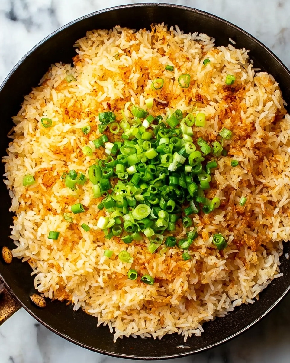A round black pan filled with a single layer of golden-brown crispy rice, with some white rice grains visible around the edges. In the center of the rice, there is a small pile of chopped green onions adding a pop of bright green color. The pan is placed on a surface with a white marbled texture. The rice looks crunchy and well-cooked, with a mix of light and darker toasted spots. Photo taken with an iphone --ar 4:5 --v 7