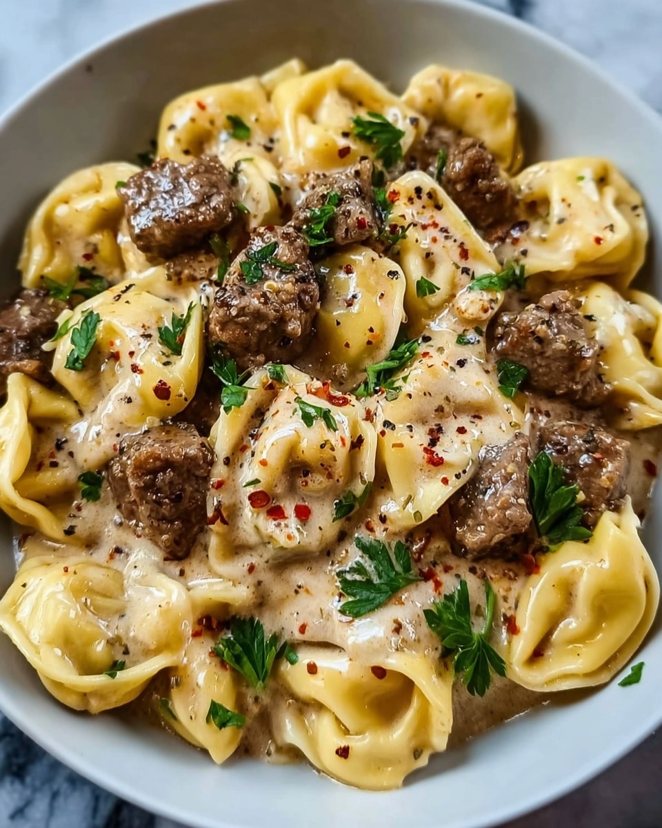 The dish shows a close-up of a white bowl filled with creamy cheese tortellini, each piece plump and golden yellow with visible folds. On top, there are many small chunks of browned beef, seared to a dark crust with a tender inside. A thick, white cream sauce covers part of the pasta and meat, with a smooth and rich texture. Small green herb pieces are sprinkled over everything, adding a pop of color, along with tiny bits of red chili. The bowl sits on a white marbled surface. photo taken with an iphone --ar 4:5 --v 7