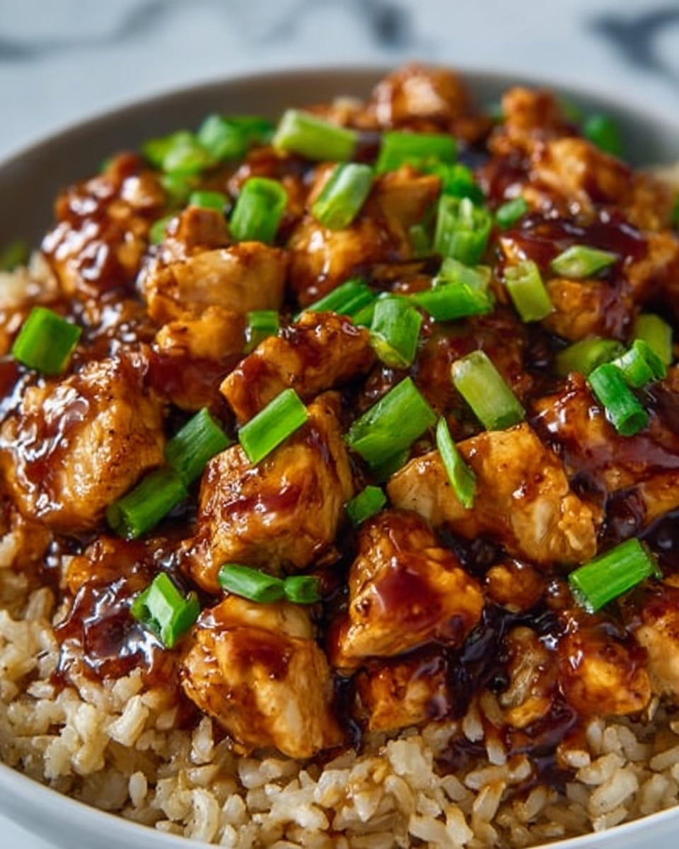 The image shows a close-up of a dish with a base layer of light brown cooked rice, topped with pieces of grilled chicken covered in a thick, glossy dark brown sauce. The chicken pieces are evenly spread over the rice and garnished with chopped bright green onions, adding a fresh contrast. The dish is placed on a white plate, set against a white marbled surface. Photo taken with an iphone --ar 4:5 --v 7