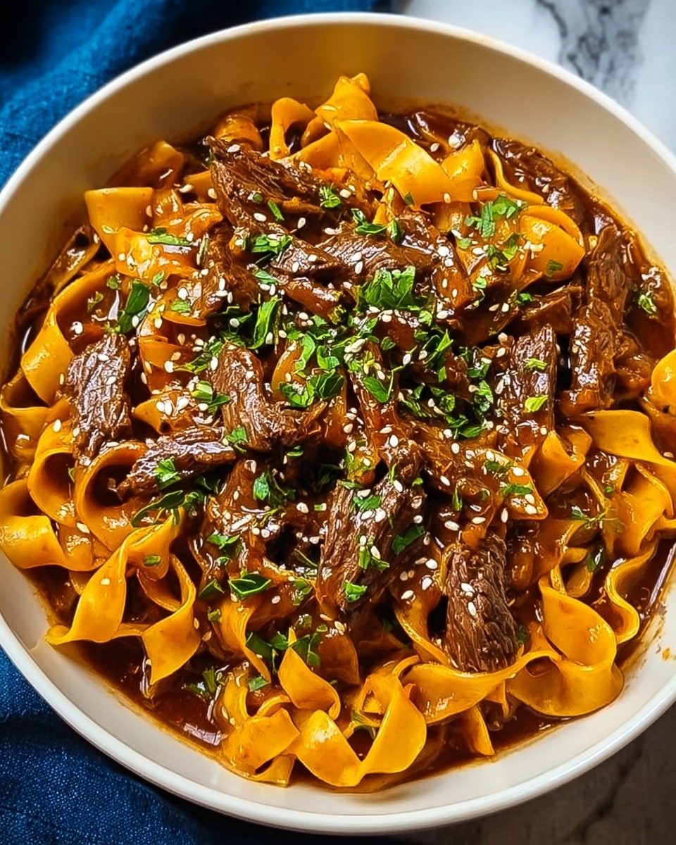 A white bowl filled with three layers: the bottom layer is wide, flat, slightly wavy noodles in a soft orange color; the middle layer is thick, rich brown sauce with a glossy texture that coats the noodles and meat; the top layer features dark brown, tender beef strips scattered throughout and garnished with fresh, bright green chopped herbs and small white sesame seeds. The bowl is set on a white marbled surface with a deep blue cloth partially visible on the side. Photo taken with an iphone --ar 4:5 --v 7