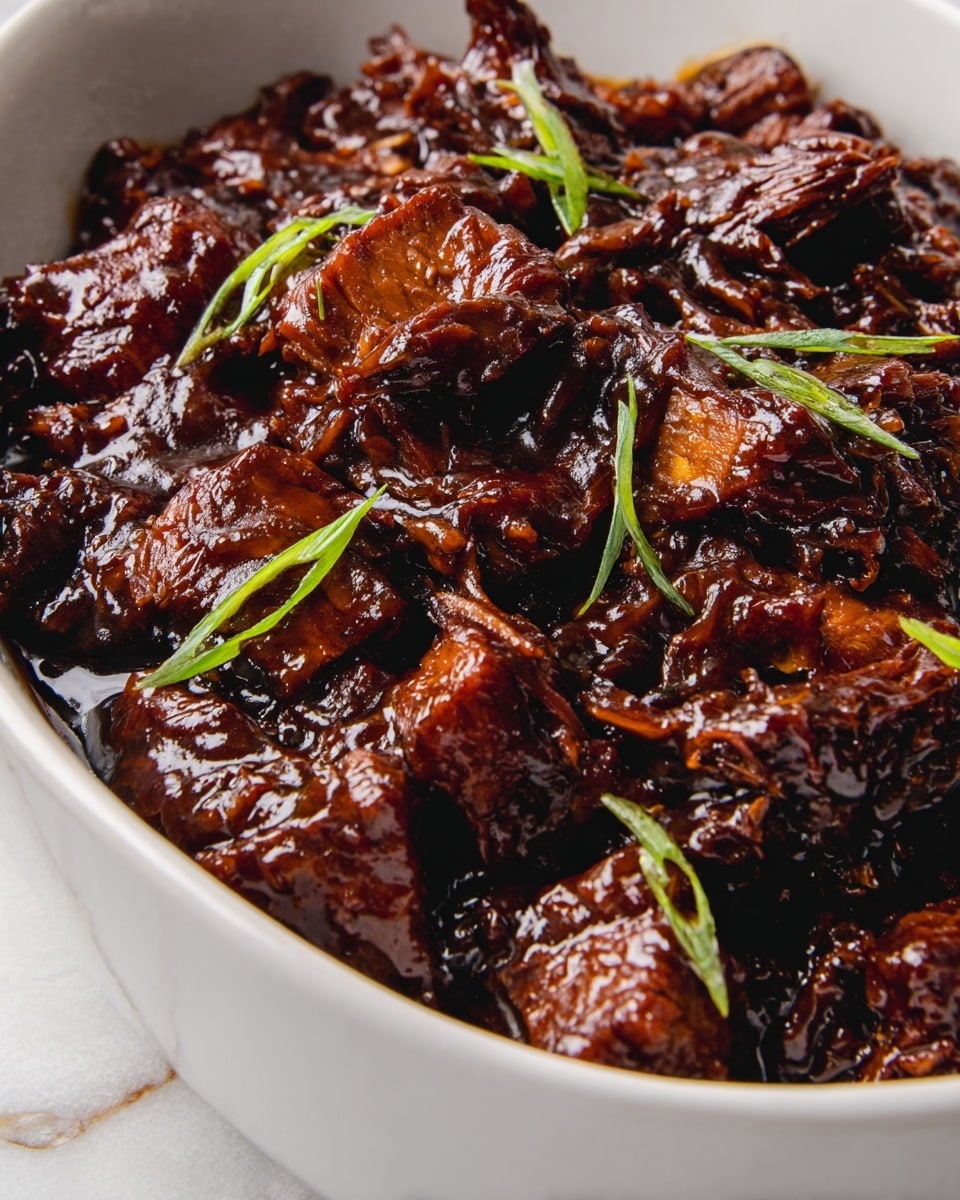 A close-up view of a white bowl filled with rich, dark brown meat pieces coated in a thick, glossy sauce that looks sticky and tender. The meat is shredded and chunky, with varied textures showing soft, juicy insides and slightly crisp edges. Small green slices of scallion are scattered on top, adding a fresh contrast. The background is a white marbled texture, highlighting the deep colors of the dish. photo taken with an iphone --ar 4:5 --v 7