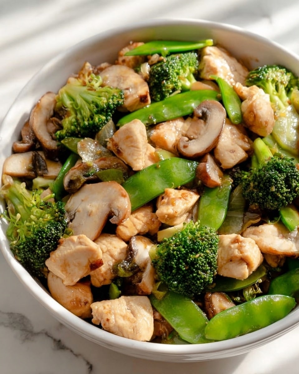 The image shows a white bowl full of a colorful stir-fry dish with three main layers. The bottom layer is a mix of green broccoli florets and bright green snap peas, showing fresh and crunchy textures. The middle layer has light beige pieces of cooked chicken, cut into small chunks with a smooth yet slightly browned surface. The top layer includes sliced brown mushrooms and white water chestnuts, adding a soft and slightly glossy texture. The dish looks fresh and healthy, placed on a white marbled surface with soft natural light. photo taken with an iphone --ar 4:5 --v 7