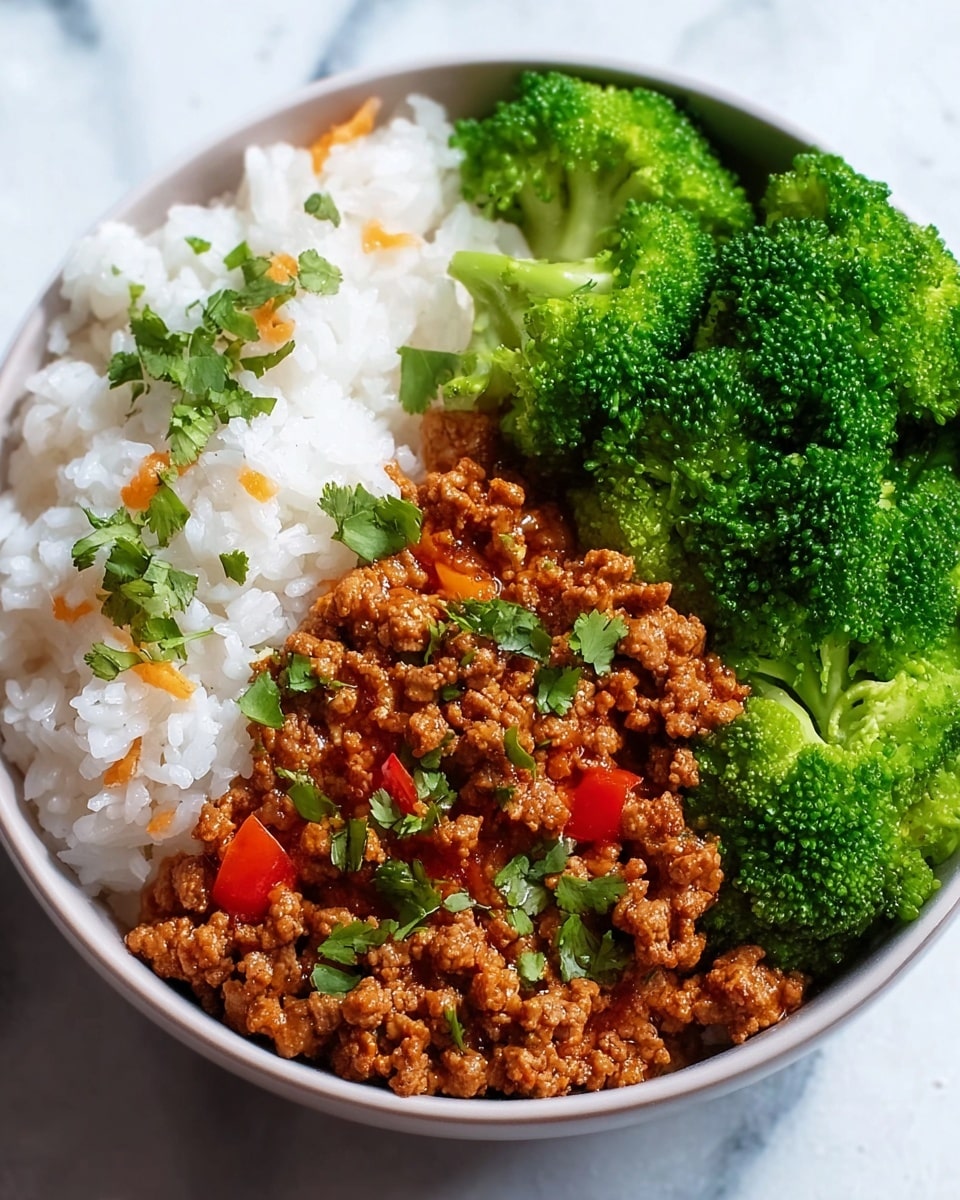 A white bowl filled with three main layers, starting on the left with a fluffy white rice layer that has small bits of orange mixed in, topped with green herb leaves scattered on top. Next to the rice, in the middle, is a layer of cooked ground meat in a reddish-brown sauce with visible small pieces of red pepper, also garnished with green herbs. On the right side, there is a layer of bright green broccoli florets packed closely together, showing a textured and fresh look. The bowl is placed on a white marbled surface. Photo taken with an iphone --ar 4:5 --v 7
